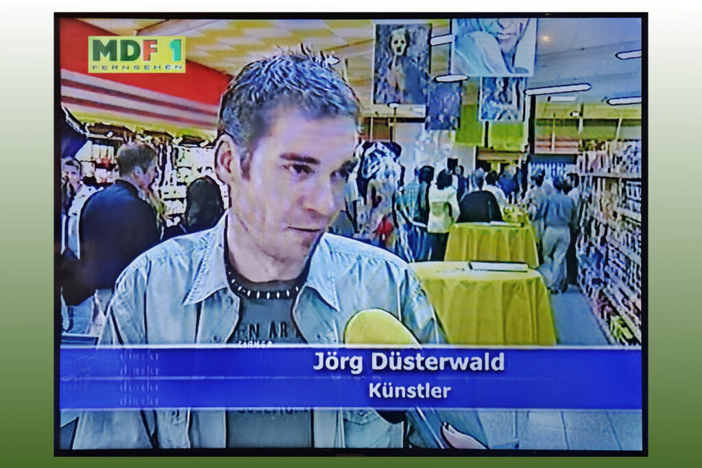 Künstler Jörg Düsterwald spricht für ein Interview in das Mikrofon eines Fernsehteams