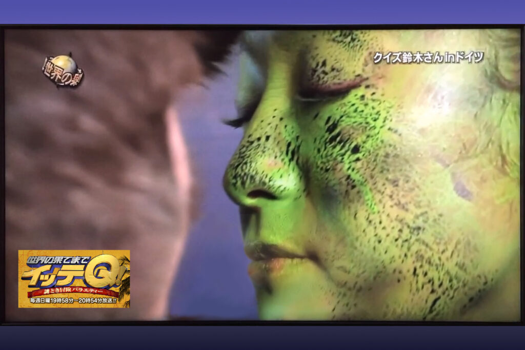 Eine japanische Entertainerin wird von Künstler Jörg Düsterwald im Gesicht mit grüner Farbe bemalt.