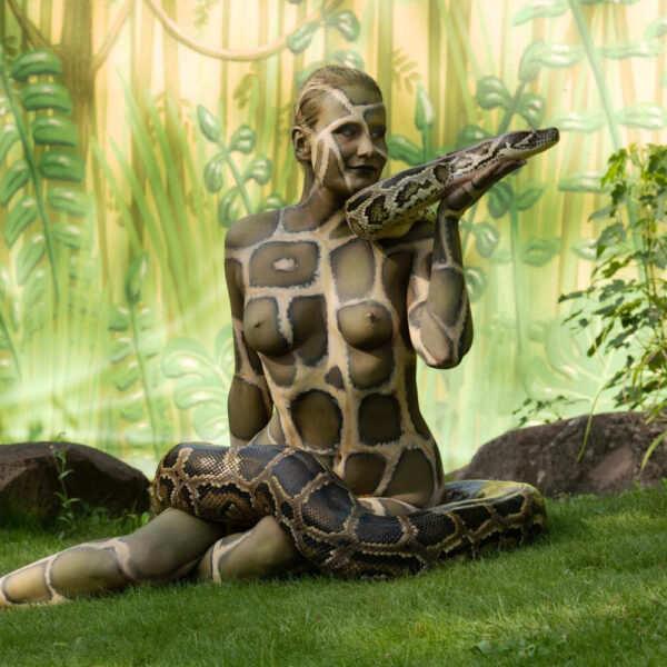 Künstler Jörg Düsterwald hat für das Kunstprojekt ANIMAL ART ein Fotomodell vollständig mit einem Schlangenmuster bemalt. In einem Zoogehege posiert die Frau für ein Fotoshooting. Um sie herum windet sich eine riesige Python-Schlange.