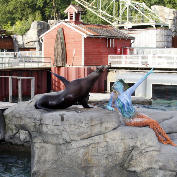 Ein von Künstler Jörg Düsterwald wie eine Nixe bemaltes Fotomodell posiert mit einem Seelöwen in einem Tiergehege in einem Zoo.