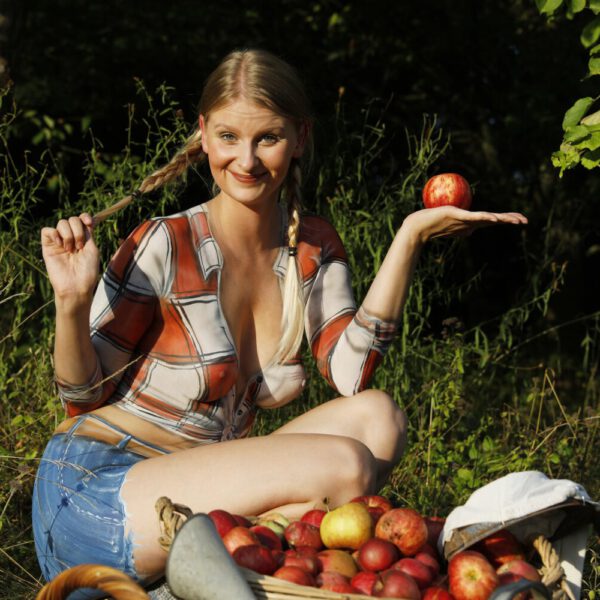 Im Rahmen des Kunstprojektes AGRAR ART hat Bodypaint-Künstler Jörg Düsterwald ein nacktes Fotomodell mit Körperfarbe so bemalt, als hätte die Frau eine kurze blaue Hose und ein rotweiß-kariertes Hemd an. Sie befindet sich in einer Apfelbaumplantage und erntet die Äpfel.
