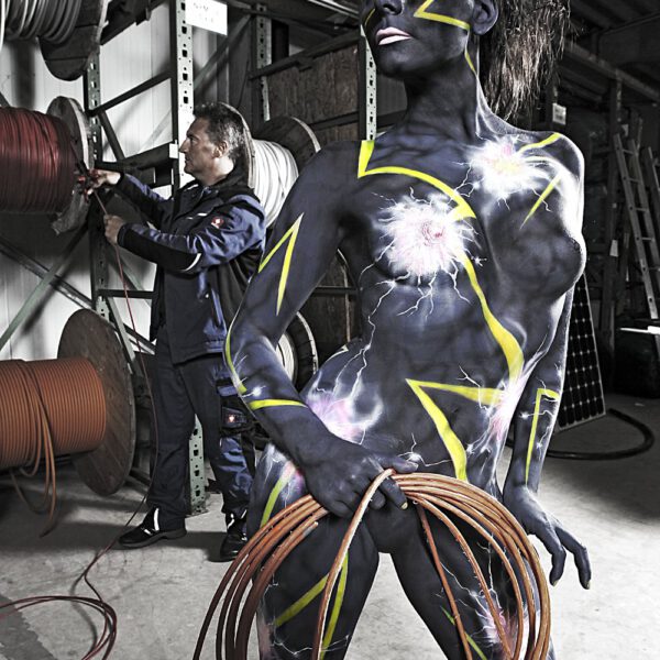 Für das Kunstprojekt WORKING ART, bei dem Berufe mit Bodypaintingmodellen dargestellt werden, hat Künstler Jörg Düsterwald ein Fotomodell vollständig bemalt. Die mit einem Elektromuster gestylte Frau hält sich zusammen mit einem Elektriker in seinem Kabellager auf.