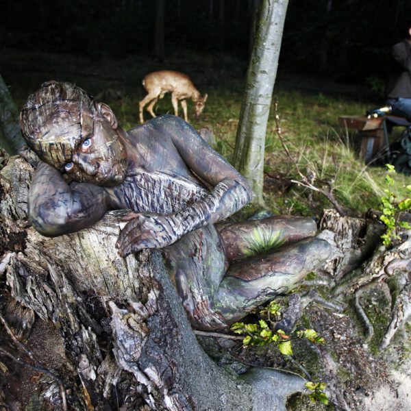 Für das Kunstprojekt WORKING ART, bei dem Berufe mit Bodypaintingmodellen dargestellt werden, hat Künstler Jörg Düsterwald ein Fotomodell vollständig bemalt. Die wie eine Baumwurzel gestylte Frau hält sich zusammen mit einem Jäger in einem Waldstück auf.