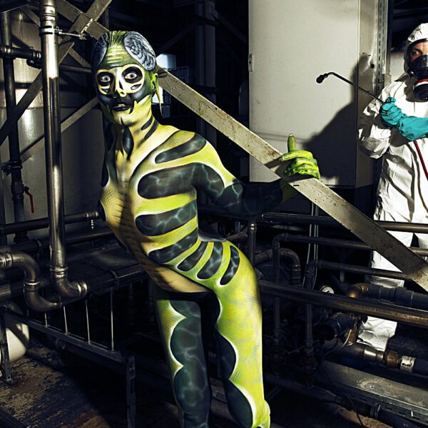 Für das Kunstprojekt WORKING ART, bei dem Berufe mit Bodypaintingmodellen dargestellt werden, hat Künstler Jörg Düsterwald ein Fotomodell vollständig bemalt. Die grün gestylte Frau sieht aus wie ein Insekt und hält sich zusammen mit einem Schädlingsbekämpfer in einer Industrieanlage auf.