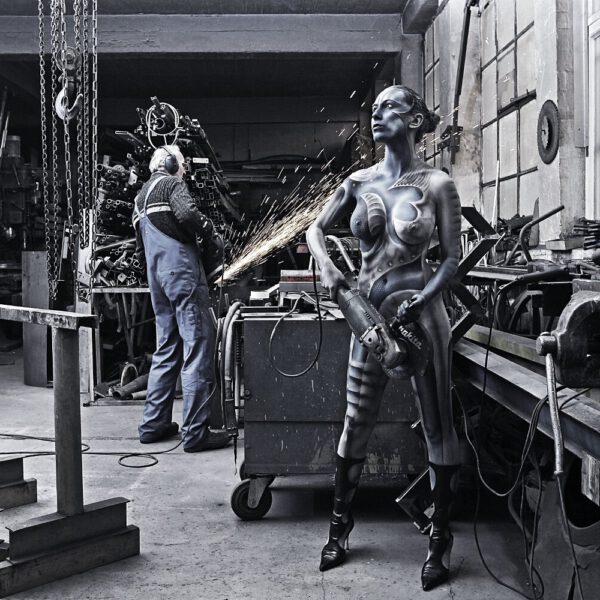 Für das Kunstprojekt WORKING ART, bei dem Berufe mit Bodypaintingmodellen dargestellt werden, hat Künstler Jörg Düsterwald ein Fotomodell vollständig bemalt. Die metallisch gestylte Frau hält sich zusammen mit einem Metallbau-Handwerker in dessen Schlosserwerkstatt auf.