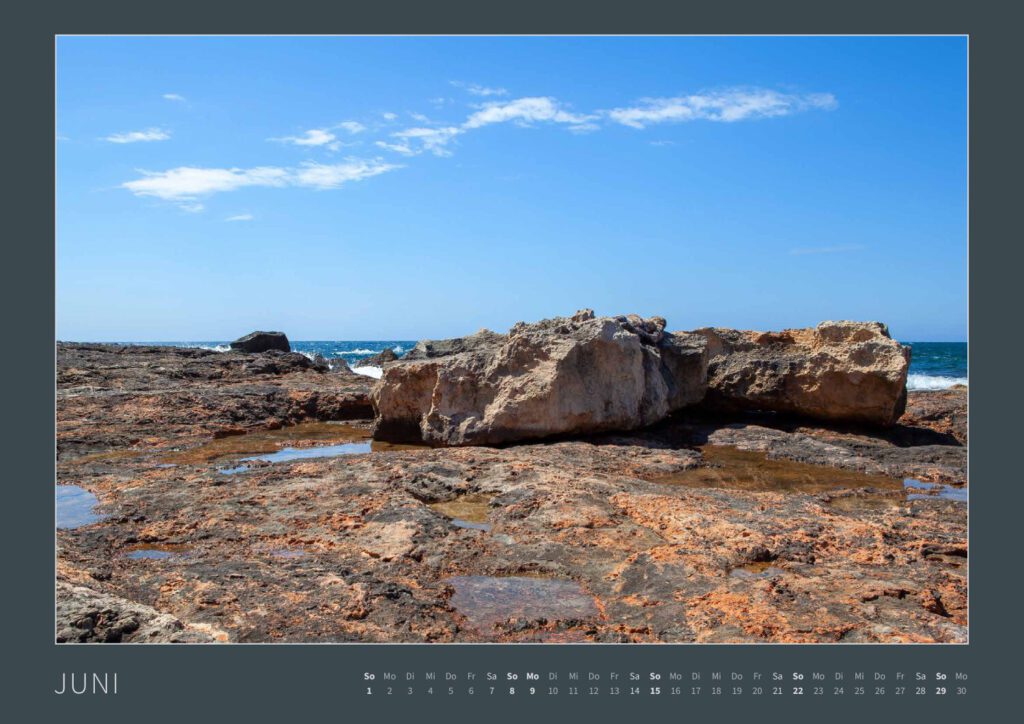 Das Monatsblatt Juni vom Bodypainting-Kalender NATURE ART 2025 von Künstler Jörg Düsterwald. Ein bemaltes Fotomodell liegt auf einem Felsen an der Mittelmeerküste der Insel Mallorca.