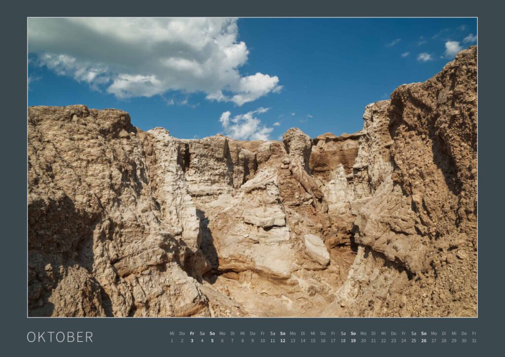 Das Monatsblatt Oktober vom Bodypainting-Kalender NATURE ART 2025 von Künstler Jörg Düsterwald. Ein bemaltes Fotomodell liegt in einer zerklüfteten Sandlandschaft.