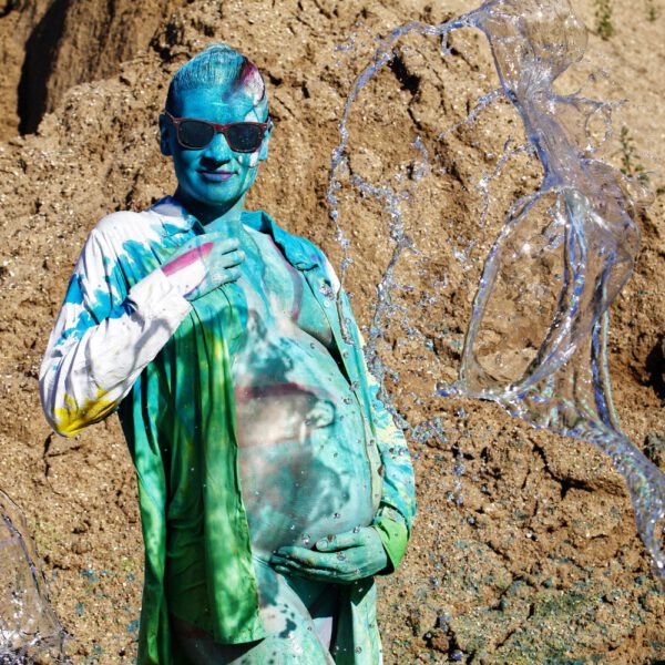 Für das Outdoor-Projekt SPLASH ART hat Künstler Jörg Düsterwald ein schwangeres Fotomodell mit Körperfarbe bemalt und anschließend in einem Sandabaugelände mit flüssiger Farbe und Wasser übergossen.