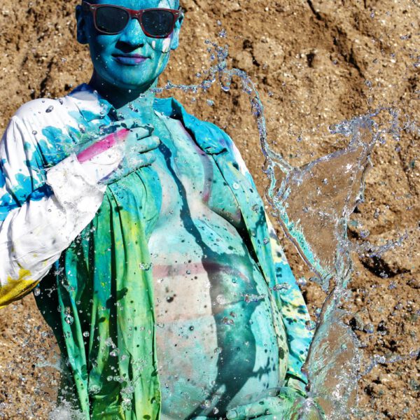 Für das Outdoor-Projekt SPLASH ART hat Künstler Jörg Düsterwald ein schwangeres Fotomodell mit Körperfarbe bemalt und anschließend in einem Sandabaugelände mit flüssiger Farbe und Wasser übergossen.