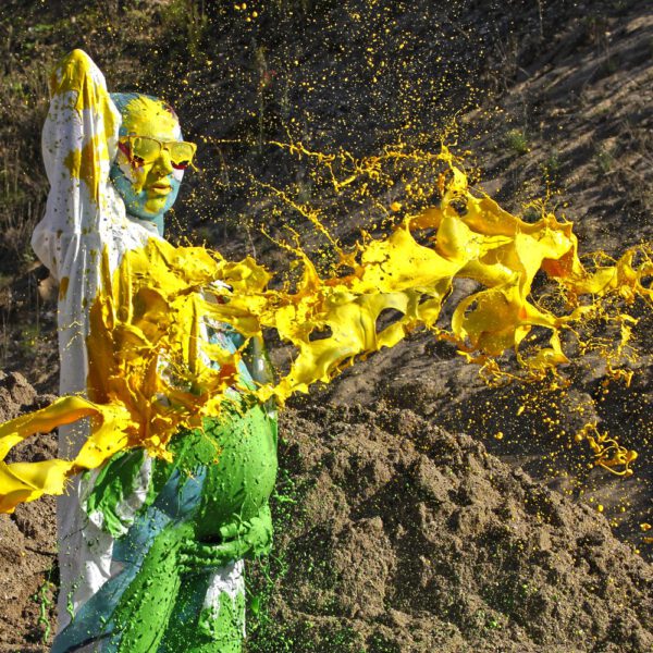 Für das Outdoor-Projekt SPLASH ART hat Künstler Jörg Düsterwald ein schwangeres Fotomodell mit Körperfarbe bemalt und anschließend in einem Sandabaugelände mit flüssiger Farbe übergossen.