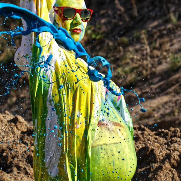 Für das Outdoor-Projekt SPLASH ART hat Künstler Jörg Düsterwald ein schwangeres Fotomodell mit Körperfarbe bemalt und anschließend in einem Sandabaugelände mit flüssiger Farbe übergossen.