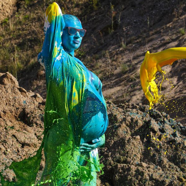 Für das Outdoor-Projekt SPLASH ART hat Künstler Jörg Düsterwald ein schwangeres Fotomodell mit Körperfarbe bemalt und anschließend in einem Sandabaugelände mit flüssiger Farbe übergossen.