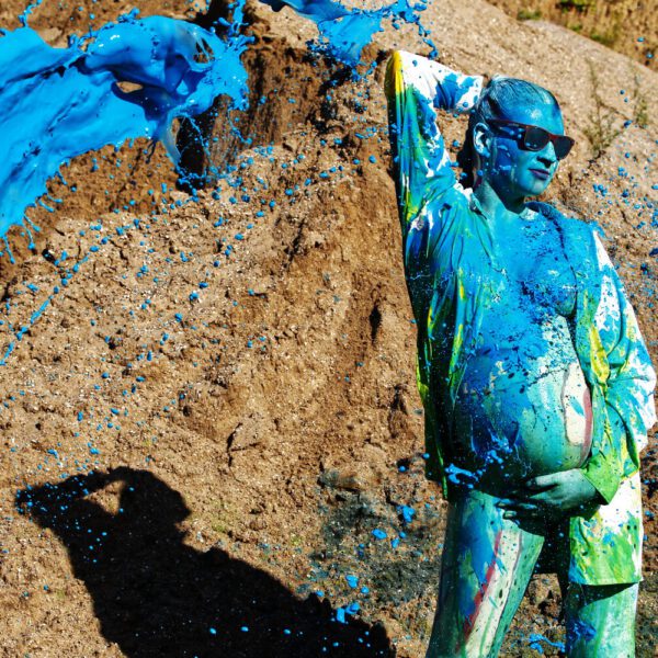 Für das Outdoor-Projekt SPLASH ART hat Künstler Jörg Düsterwald ein schwangeres Fotomodell mit Körperfarbe bemalt und anschließend in einem Sandabaugelände mit flüssiger Farbe übergossen.