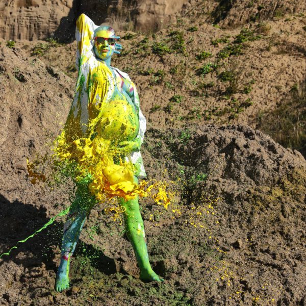 Für das Outdoor-Projekt SPLASH ART hat Künstler Jörg Düsterwald ein schwangeres Fotomodell mit Körperfarbe bemalt und anschließend in einem Sandabaugelände mit flüssiger Farbe übergossen.